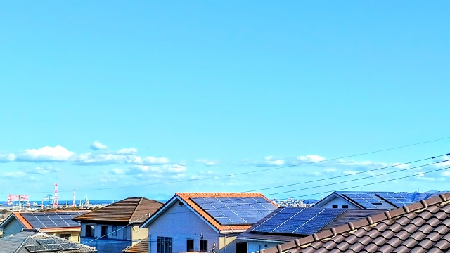 住宅街の屋根に設置された太陽光パネルと広がる青空

