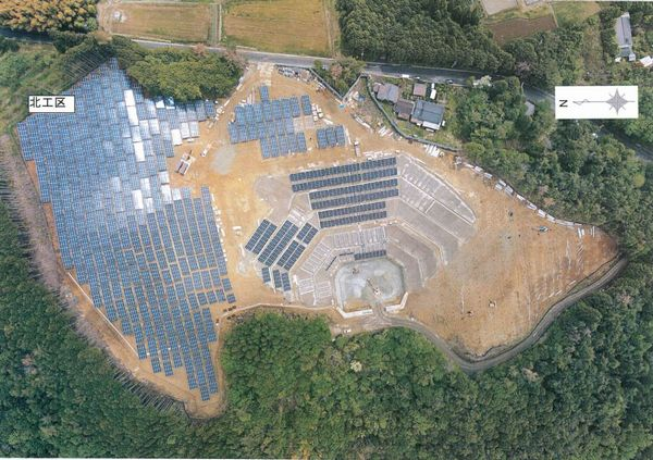 森林に囲まれた太陽光発電施設の航空写真
