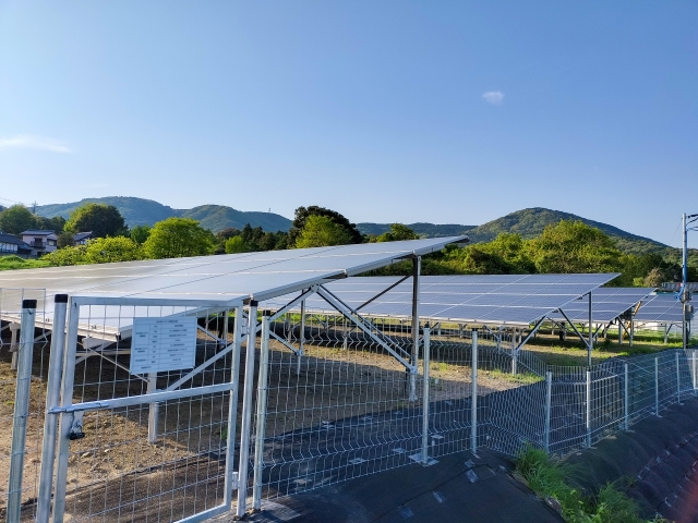 フェンスに囲まれた屋外の太陽光発電パネルと青空
